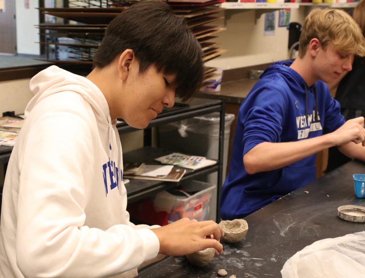 Two Westminster students mold and sculpt the bases of clay pots